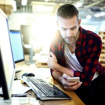man using a smartphone while sat in front of a computer